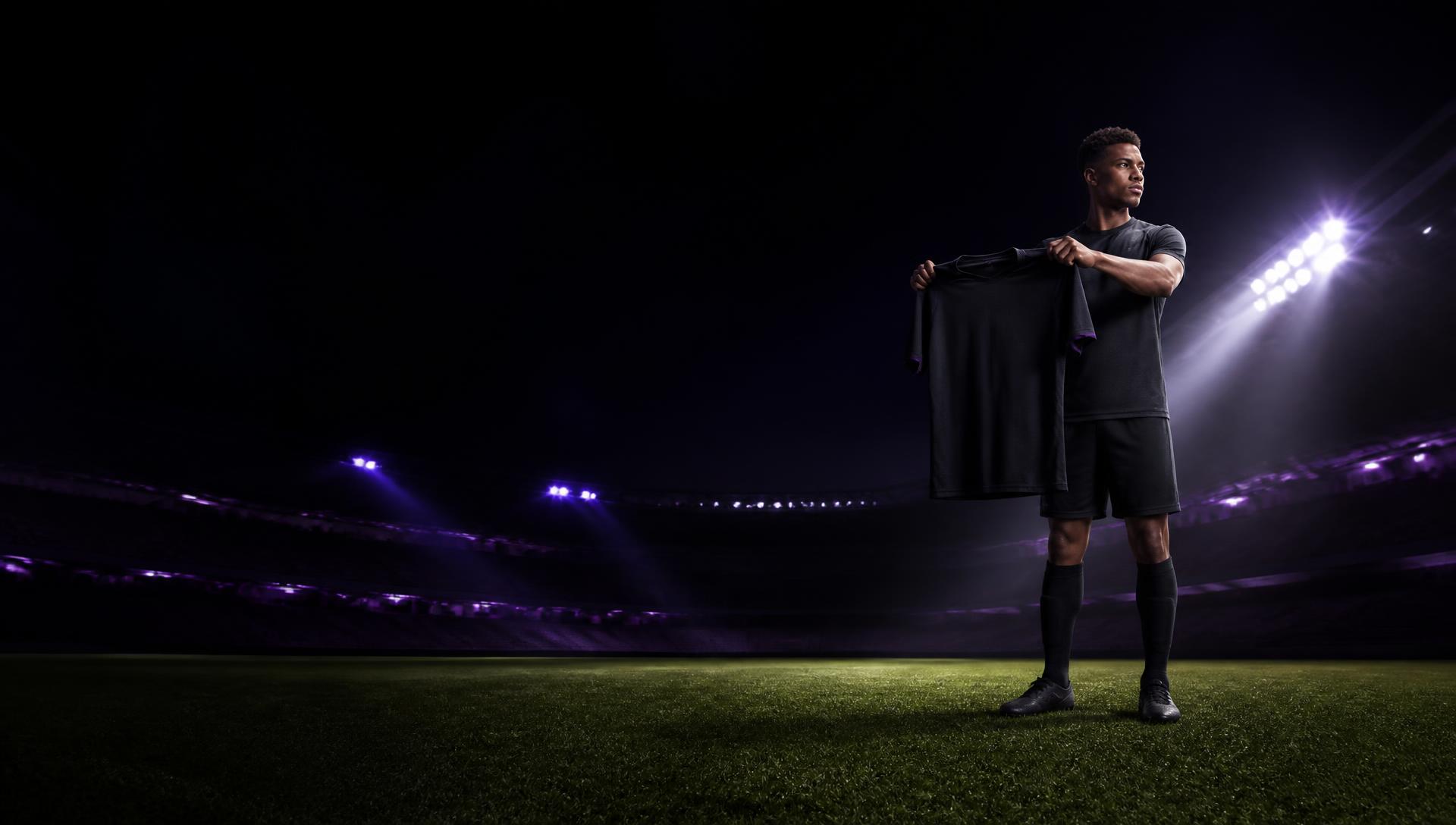 Footballer holding a custom shirt under stadium floodlights at night